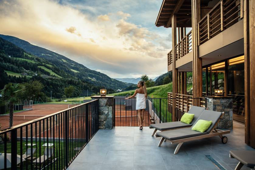Frau steht im Handtuch auf Balkon mit Blick über den Tennisplatz