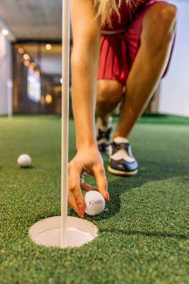 Frau legt Golfball ans Loch