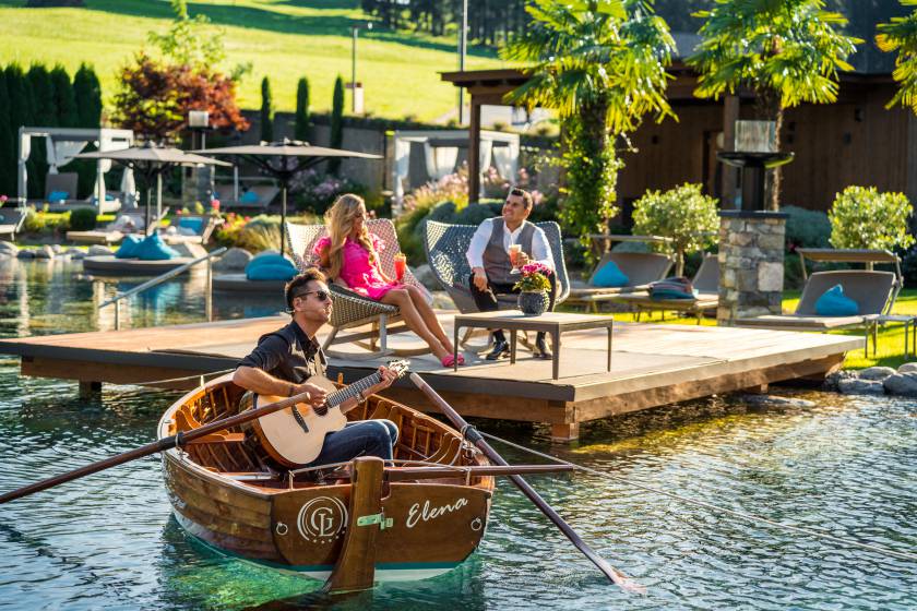 Paar entspannt auf Terrasse am Naturbadeteich mit Gitarrist im Boot