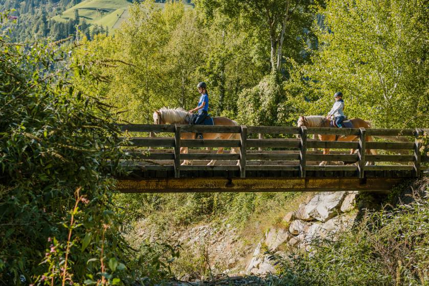 Kinder reiten mit Pferden über eine Brücke
