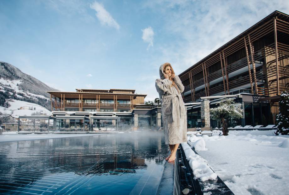 Frau im Bademantel steht am Pool im Winter