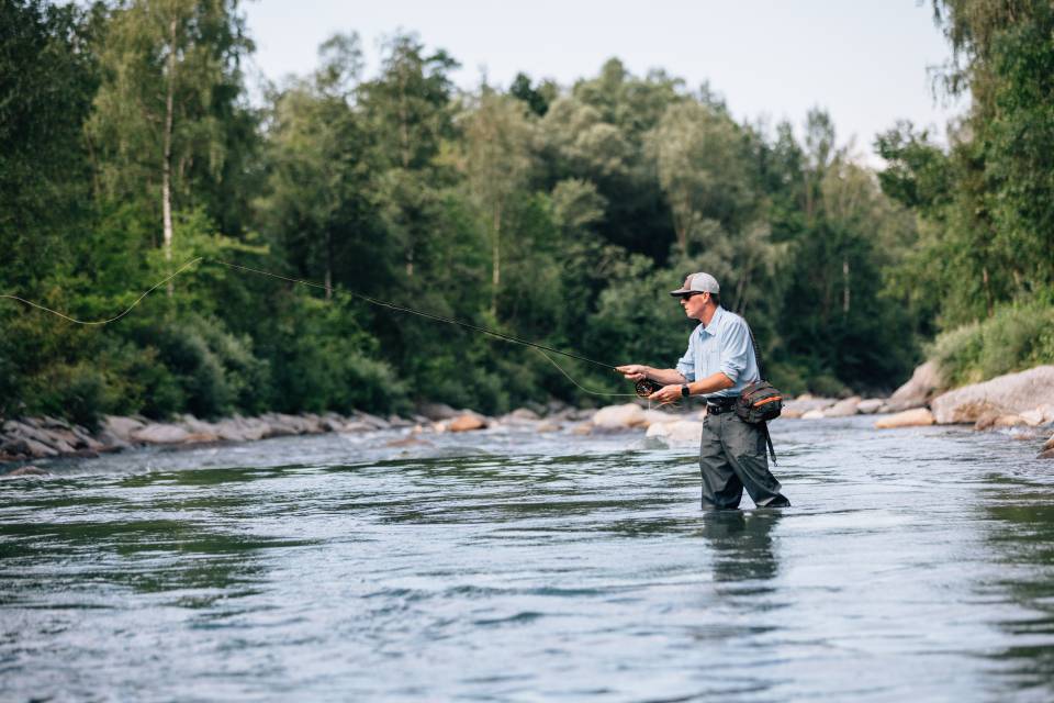 Mann steht im Fluss und Angelt in Meran